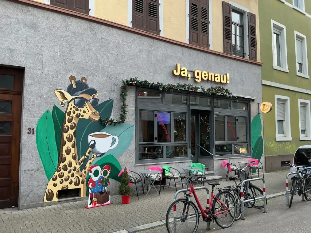 The Ja, genau! coffee-shop sign in Karlsruhe: gold 3D letters on a grey stone facade, next to a giraffe mural