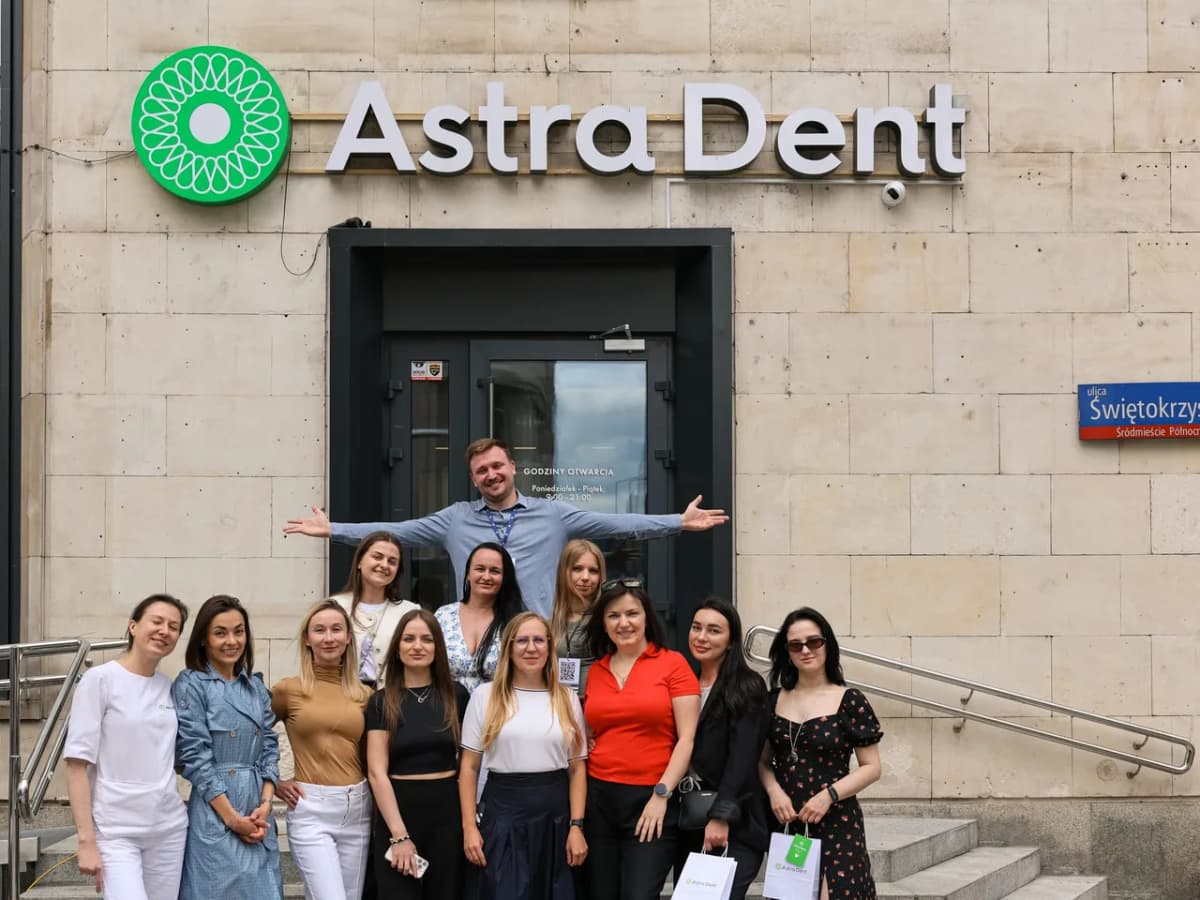 The Astra Dent team outside their Warsaw entrance: a green illuminated disc logo and white 3D letters on a stone facade