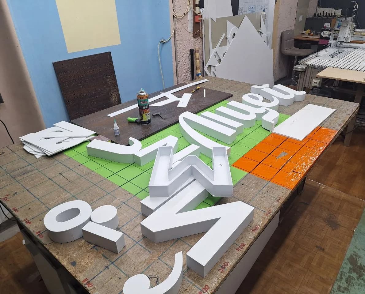 White blanks of the dimensional letters laid out on the assembly bench, the flatbed router behind them