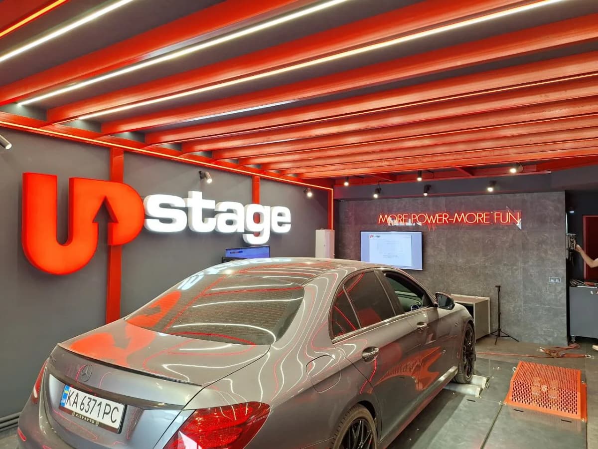 Red 3D UPstage letters on a tuning studio bay wall with a car on the dyno