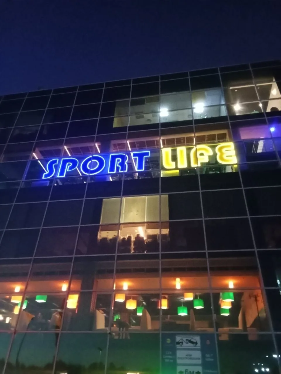 Кольорова світлова вивіска Sport Life на скляному фасаді фітнес-клубу ввечері