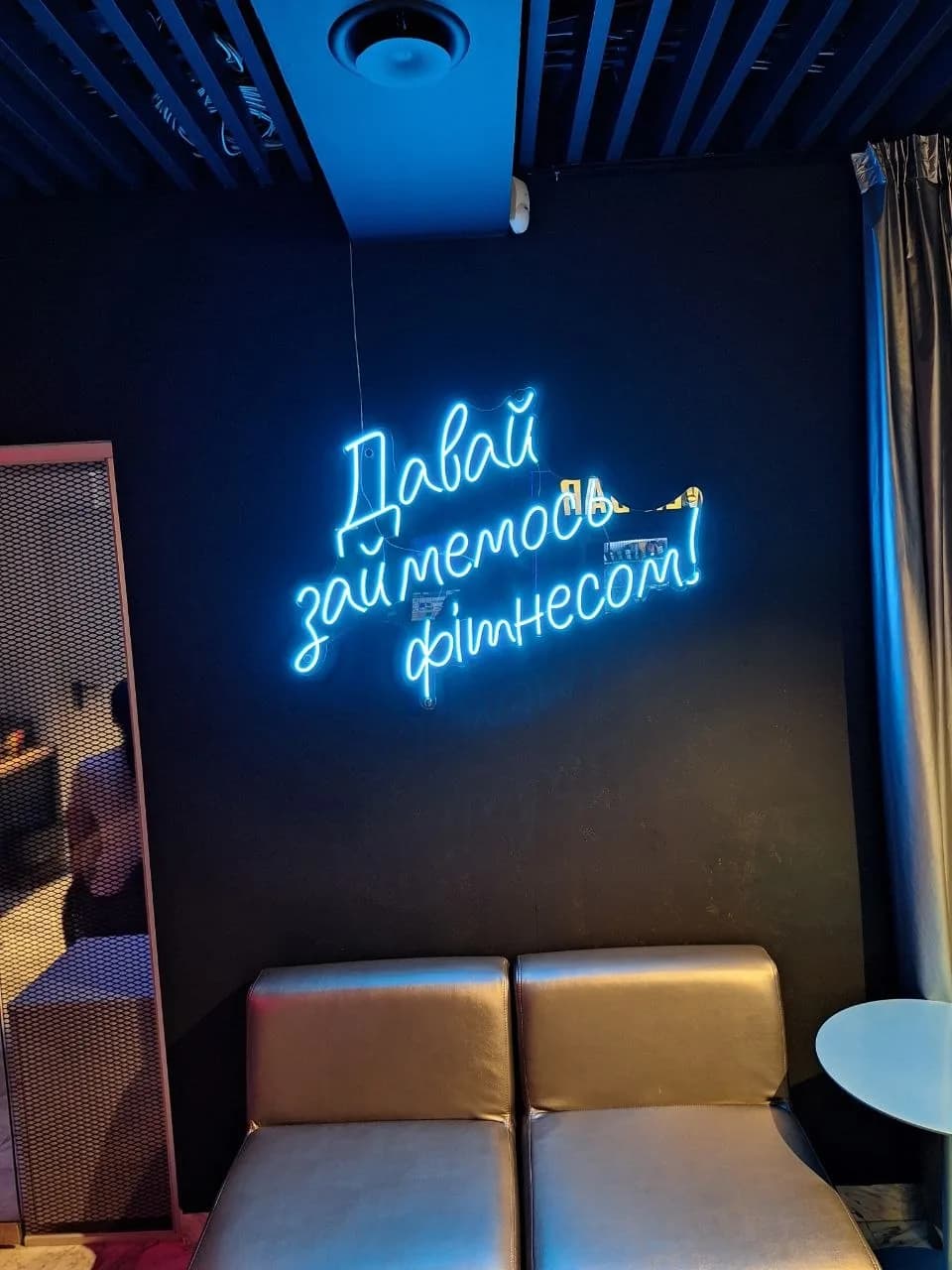 Blue neon lettering reading "Let's do some fitness!" in a gym lounge