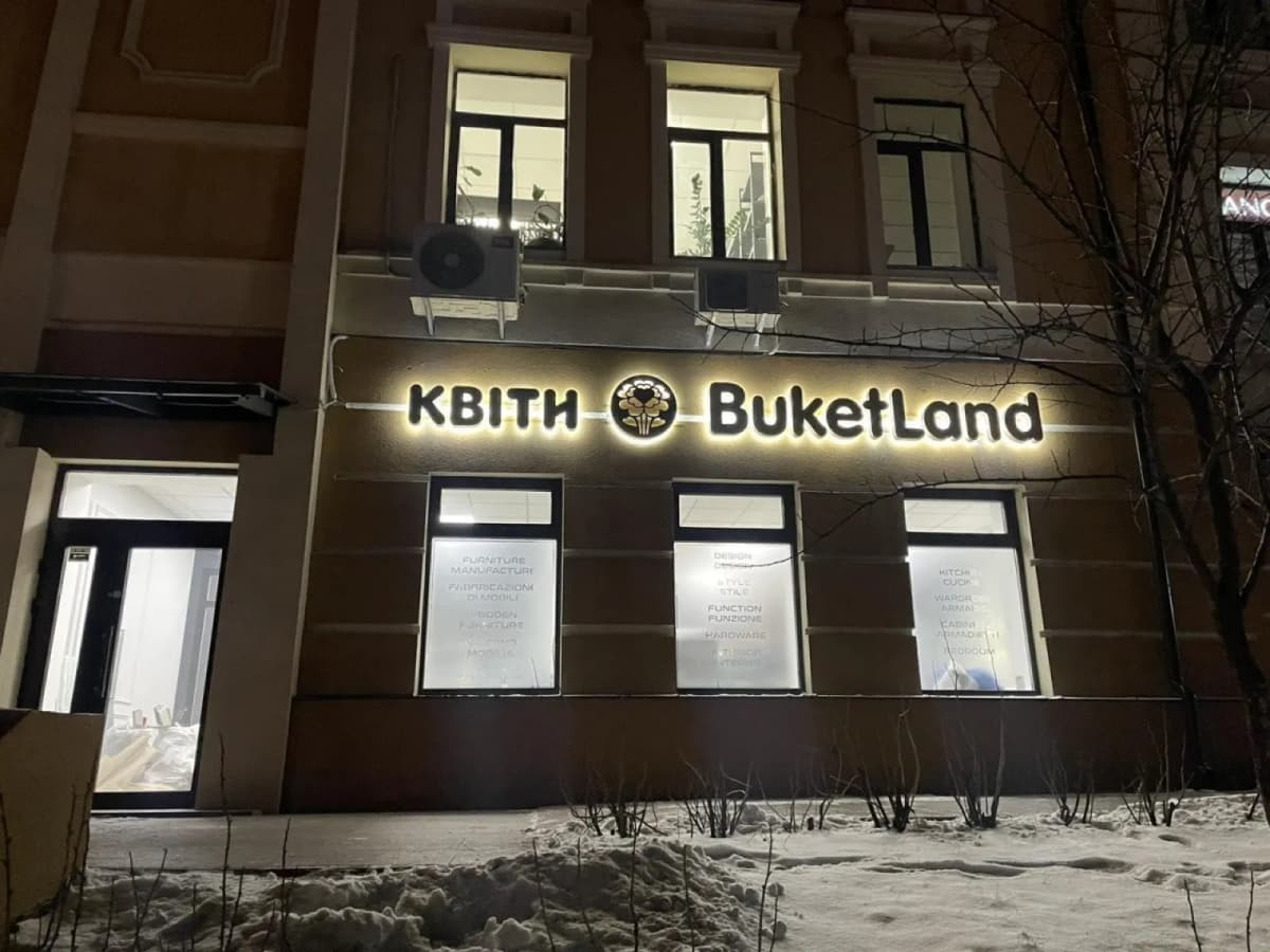Halo-lit "Kvity BuketLand" sign on a dark facade of a snow-covered building in the evening
