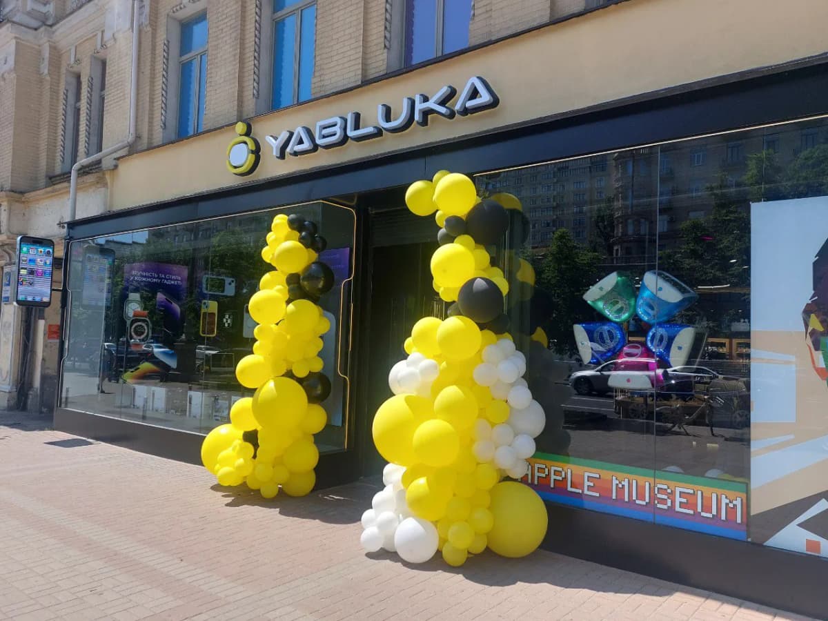 Фасад магазину YABLUKA вдень: світла вивіска над вітринами й святкові кулі біля входу