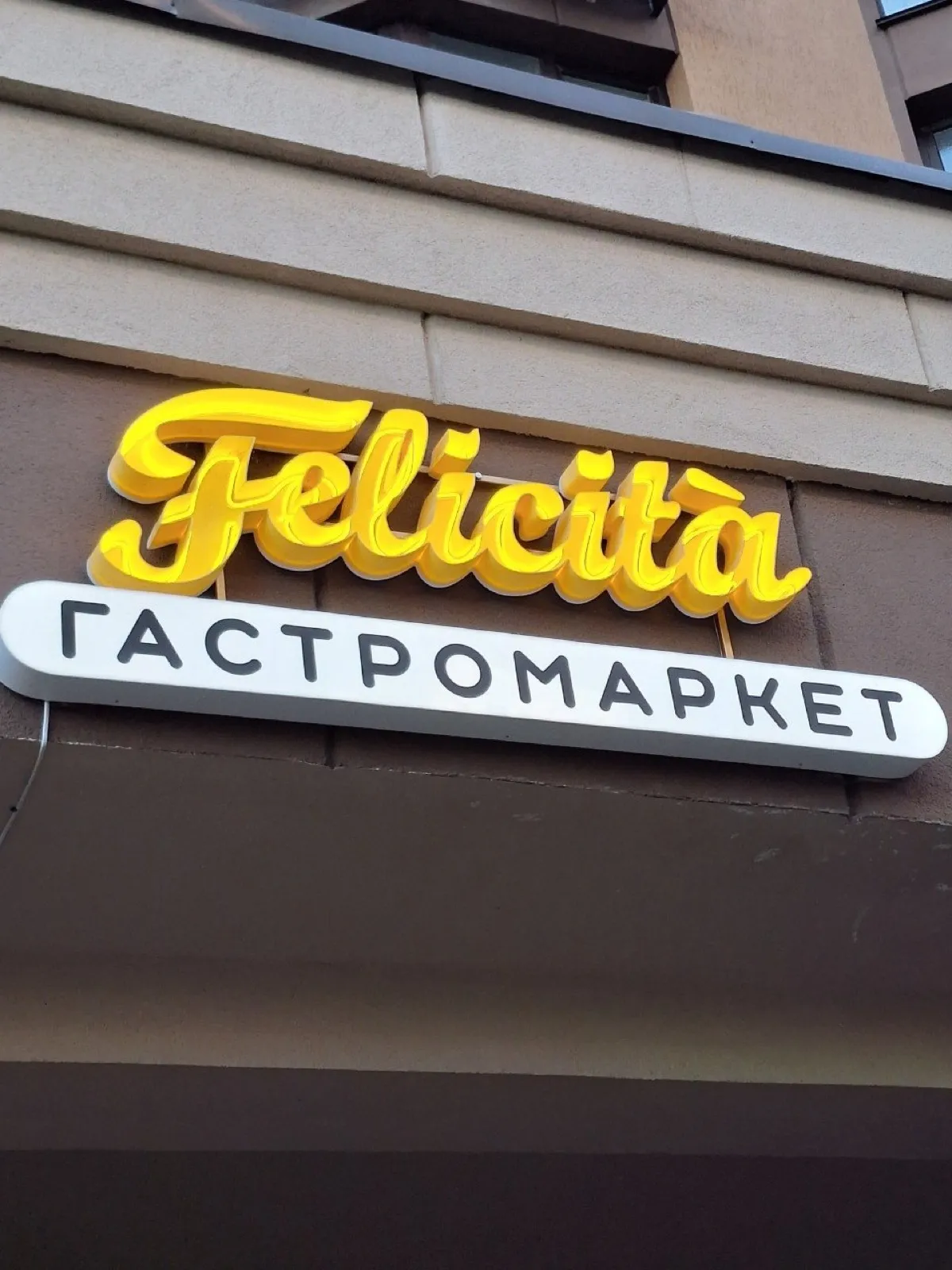 Yellow script Felicità lettering above a white oval lightbox reading "Food market"