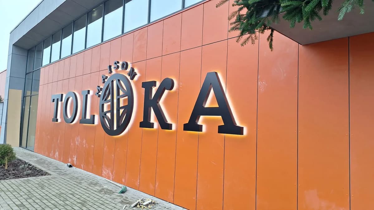 Black 3D Toloka Maison letters with a globe logo on an orange composite facade