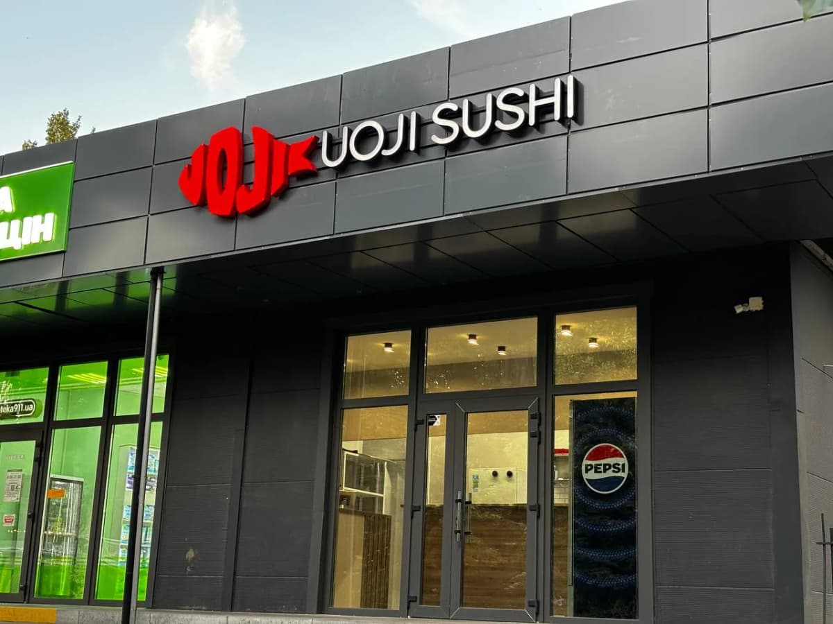 Red dimensional fish logo and white UOJI SUSHI letters on a dark grey composite facade