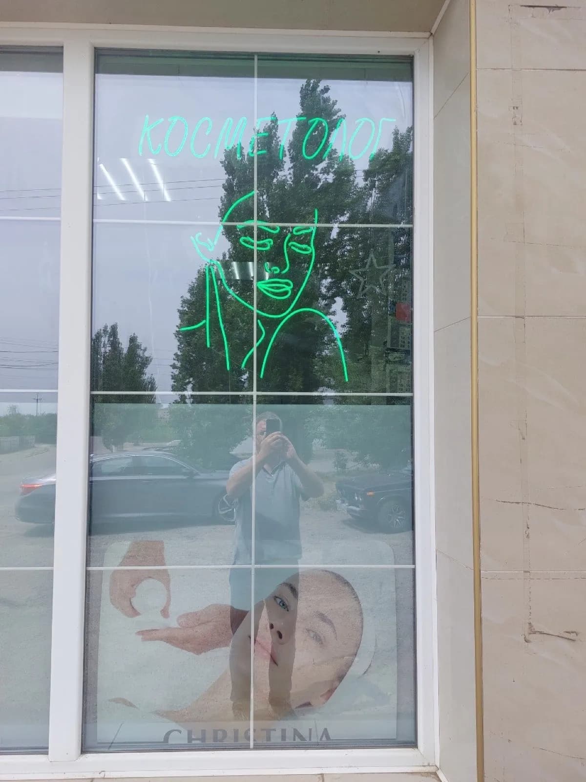 Green neon outline of a face with the word for "cosmetologist" in a studio window