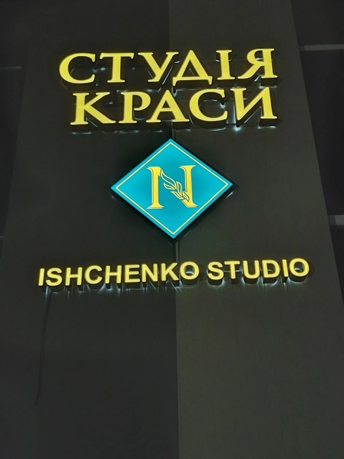 Gold 3D lettering with halo lighting and a diamond logo on a beauty studio wall at night