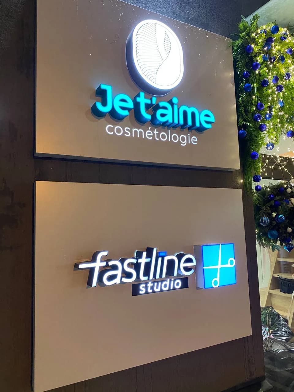 Two illuminated signs one above the other: Je t’aime cosmétologie and fastline studio on framed panels