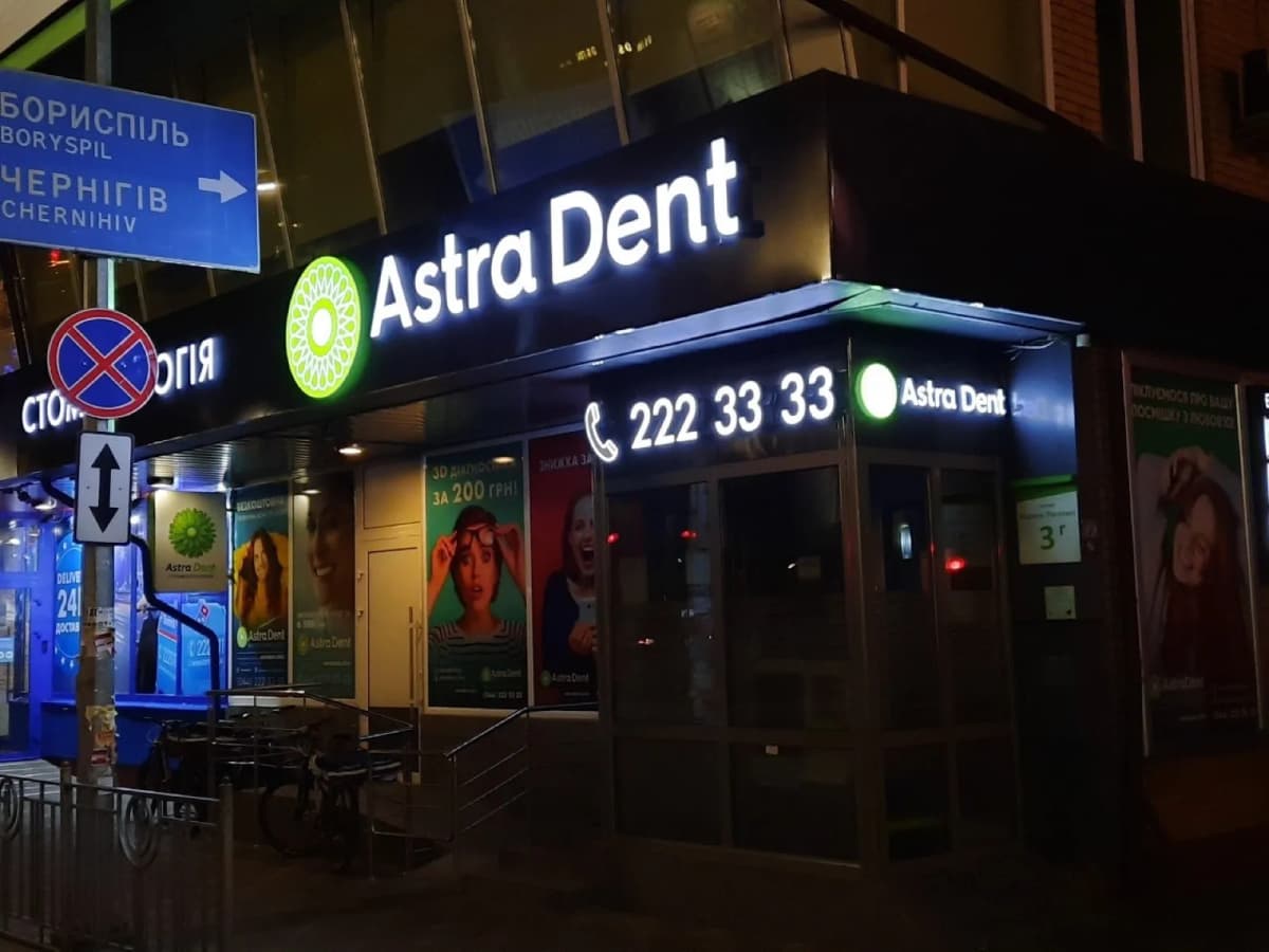 Illuminated 3D letters “Astra Dent” on a dental-clinic facade at night