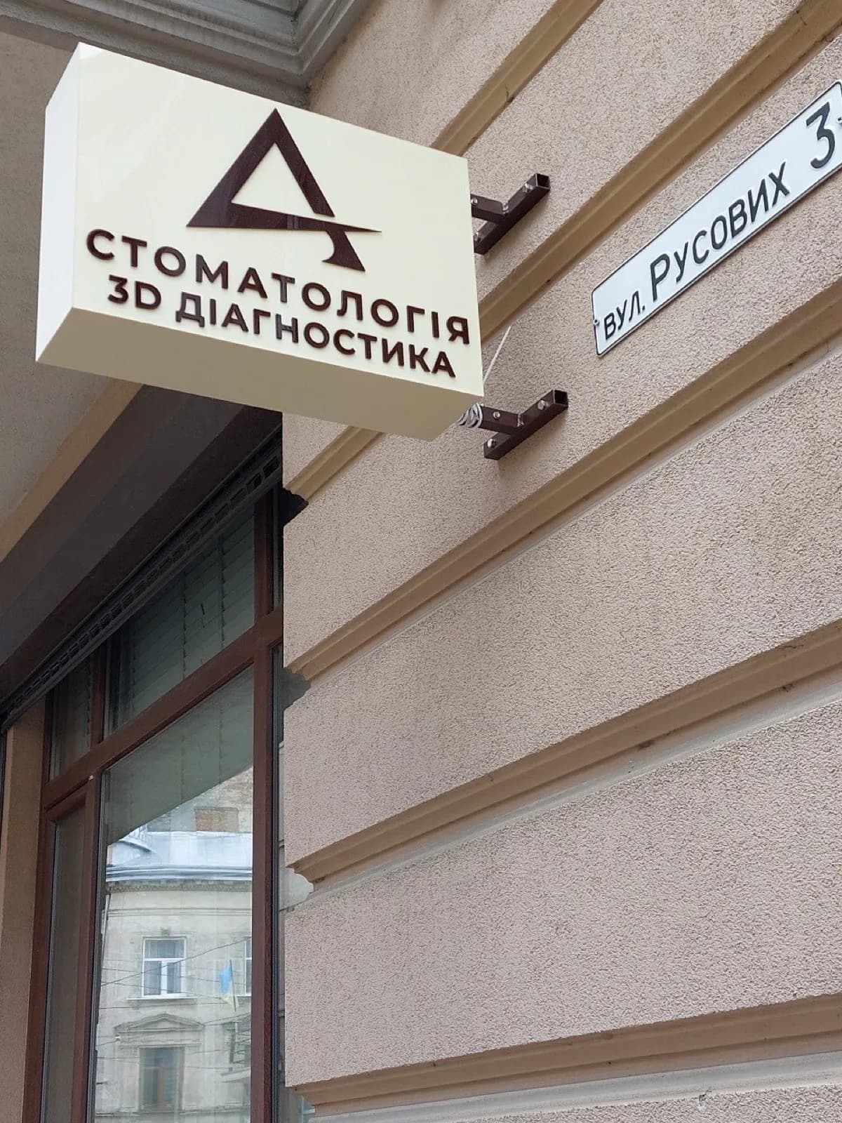 Rectangular illuminated bracket sign reading "Dentistry, 3D diagnostics" on a building facade