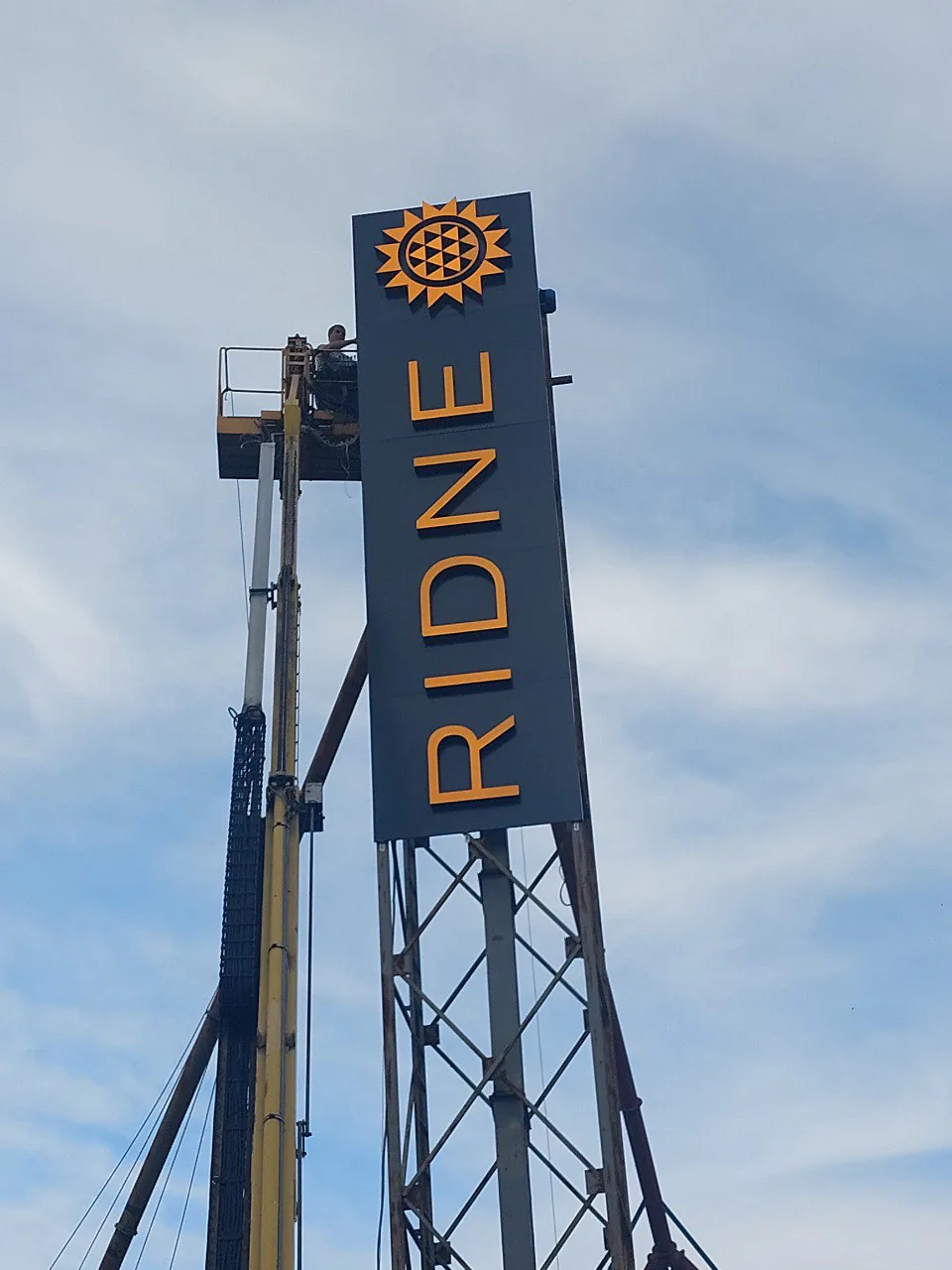 Vertical RIDNE pylon with a sunflower mark on a steel mast, an installer in a lift basket alongside