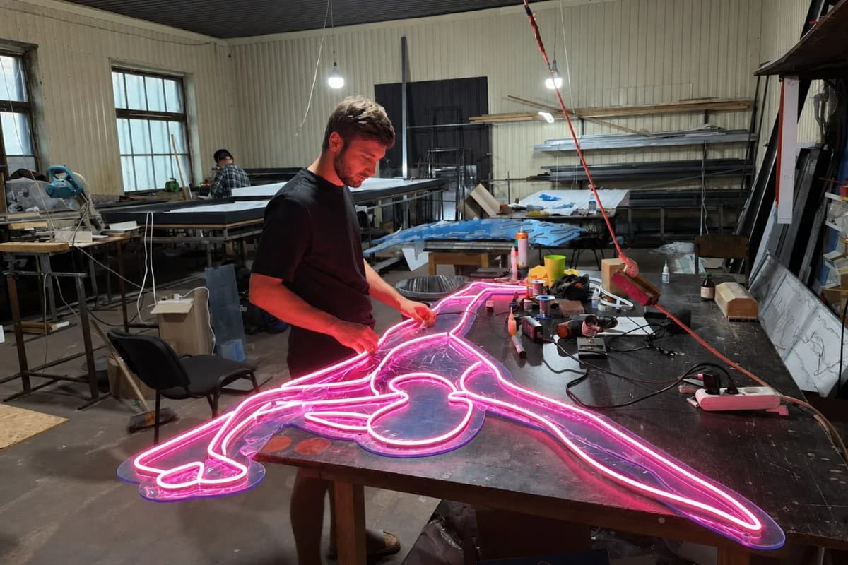A TheFace craftsman assembling a large pink neon figure on an acrylic backer
