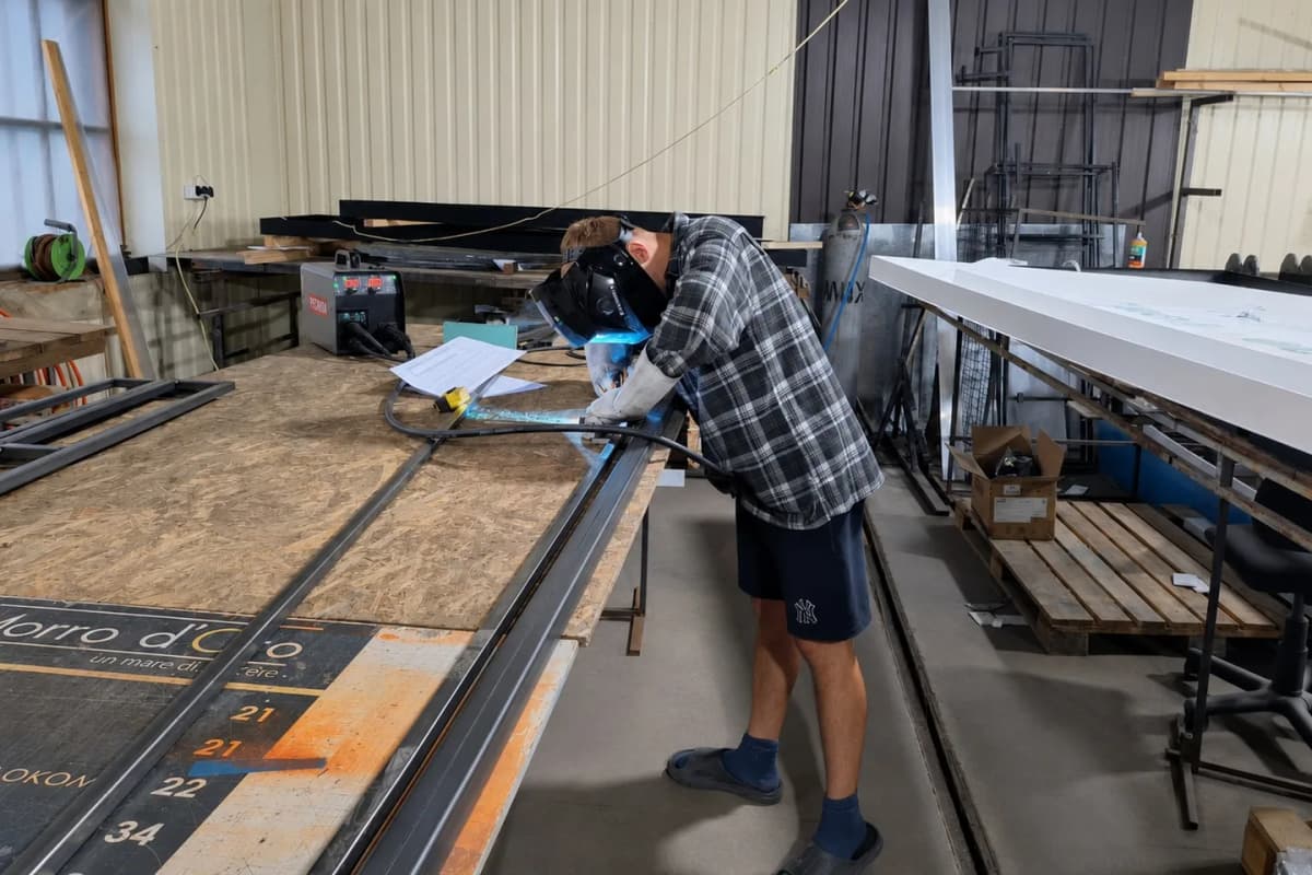 A TheFace craftsman welding a steel sign frame at the bench in the workshop